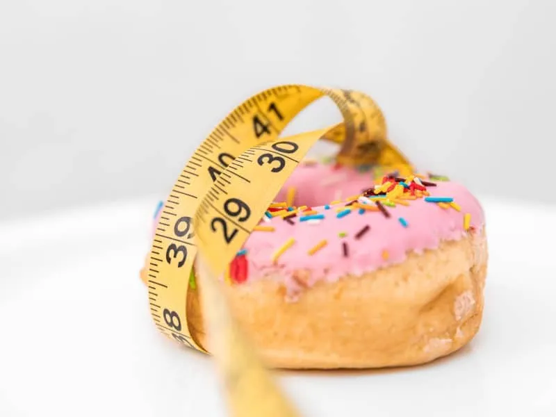 Close up of donut and measuring tape, weight loss and diet concept.