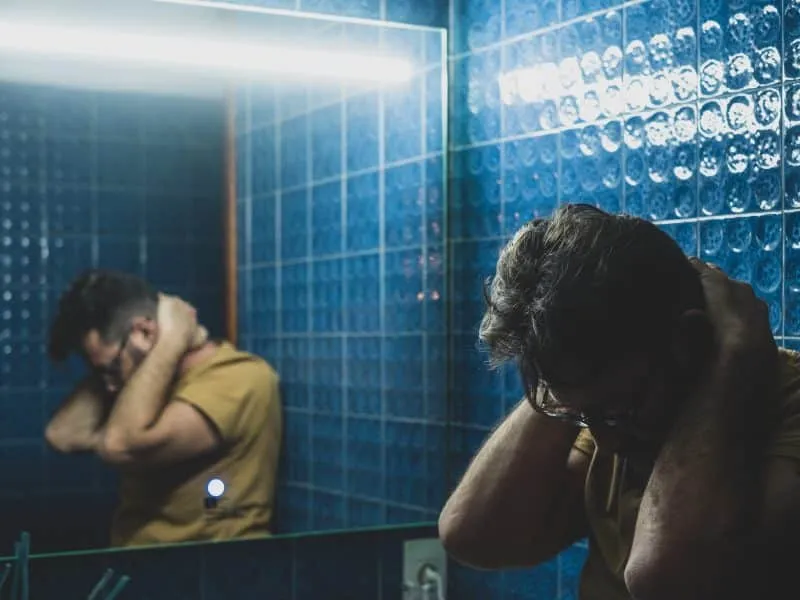 Close up of one sad depressed man looking himself in the mirror of the bathroom reflexing about his life or lifestyle. Sick male person unhappy thoughtful.