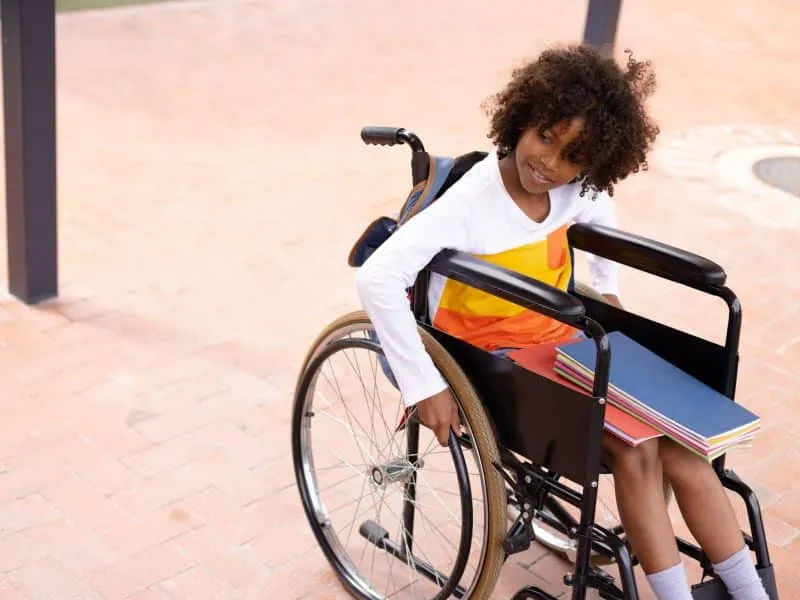 Happy african american schoolgirl in wheelchair at school. Education, inclusivity, elementary school, learning and disability concept.