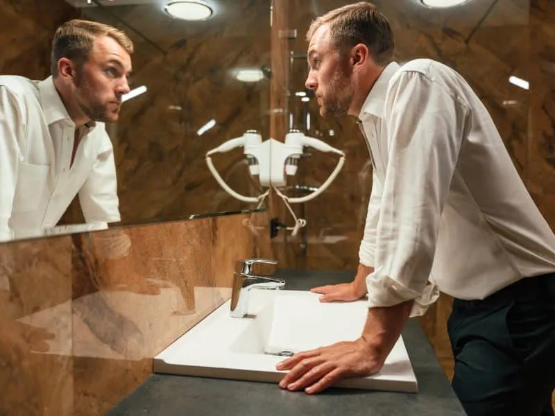 Man in formal clothes is in the bathroom against mirror.
