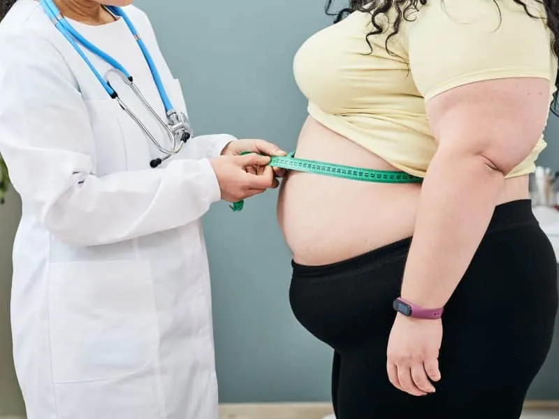 Obesity, unhealthy weight. Nutritionist inspecting a woman's waist using a meter tape to prescribe a weight loss diet