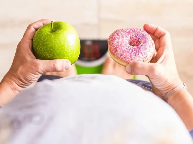 woman look at donut and apple to select her nutrition lifestyle - she's on a weight scale