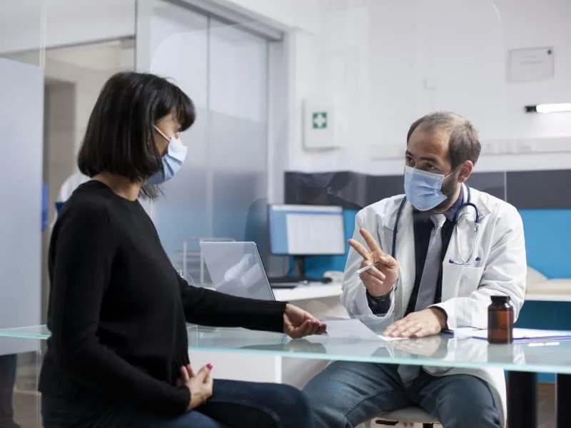 Young woman sitting at desk and receiving prescription paper from doctor during clinic appointment. Male physician giving medical document and explains treatment plan to female patient in hospital.