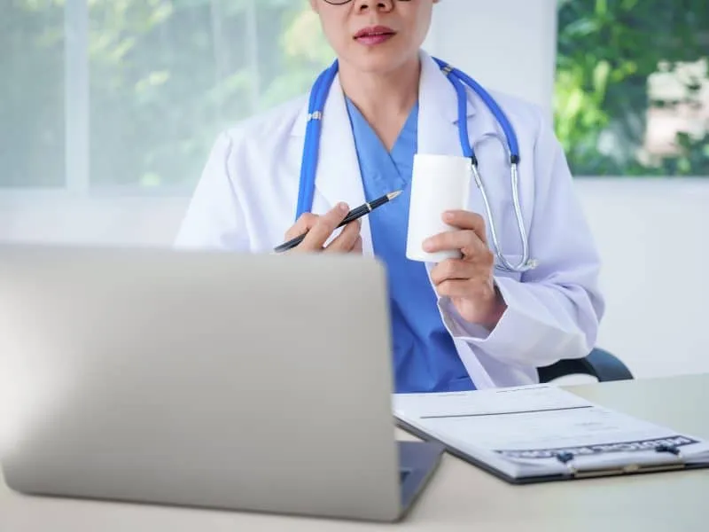 An Asian female doctor sits at her desk, conducting an online consultation. This faster, cheaper