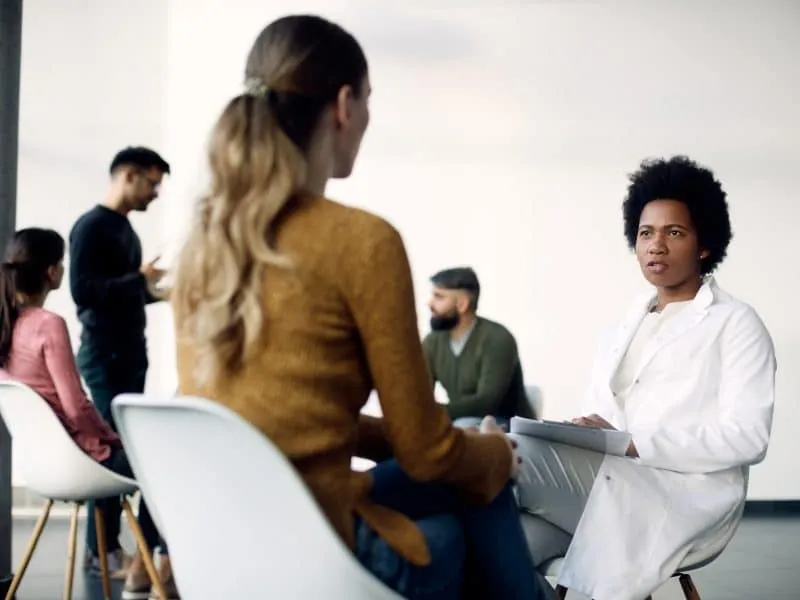 Black female counselor talking to a woman during group therapy at medical center.