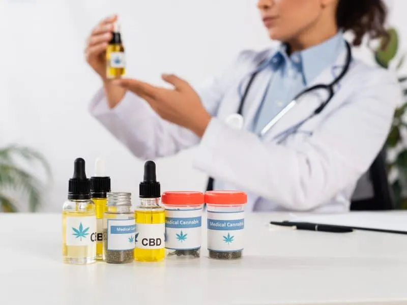 bottles with cbd and medical cannabis lettering near african american doctor on blurred background