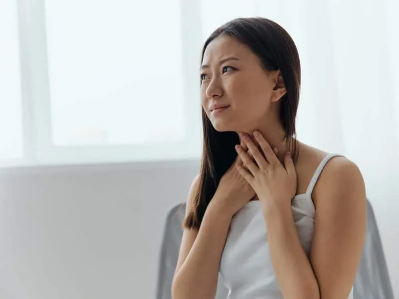 Cough Tickling. Portrait of suffering crying tanned beautiful young Asian woman touch neck sore throat at home interior living room. Injuries Poor health Illness concept. Cool offer Banner