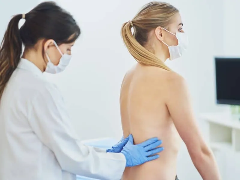 Doctor in mask checking up breast to her patient