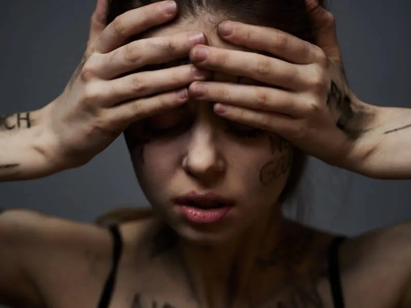 Frustrated woman with offensive inscriptions on her body and in a black T-shirt on a gray background portrait cropped view. High quality photo