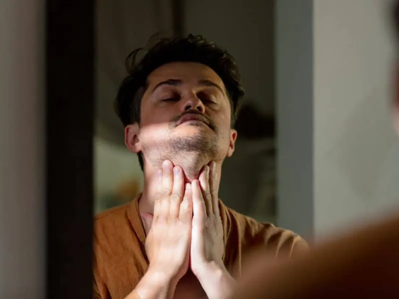 man applies hydration cream on the skin of face in bathroom near a mirror