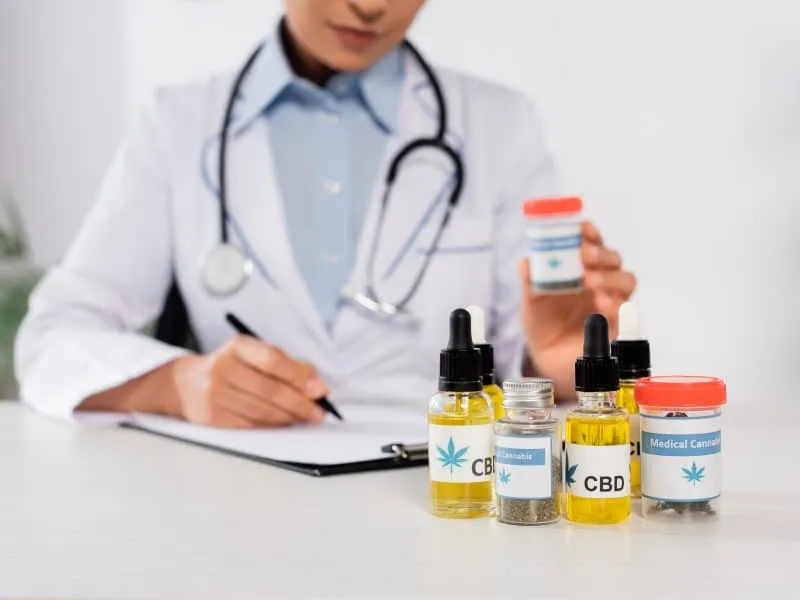 partial view of african american doctor with stethoscope holding bottle with medical cannabis