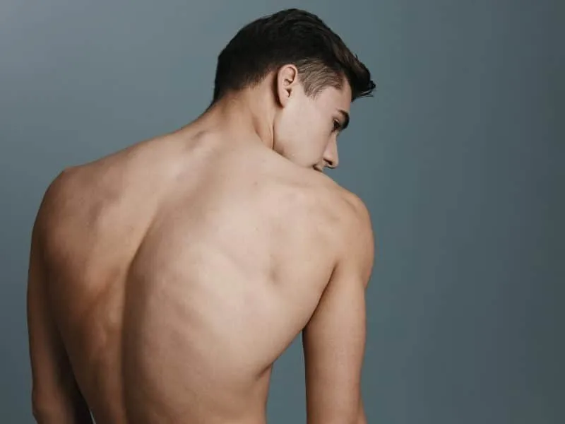 Sexy man with a naked back looks to the side against a gray background. High quality photo