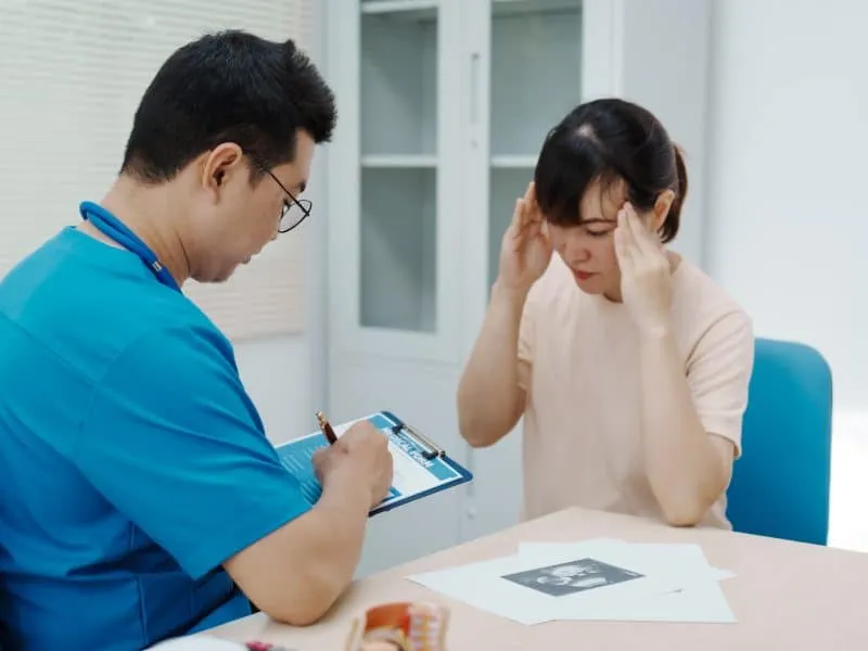 Asian male doctor listens to pregnant mother during pregnancy checkup. Doctor provides services.