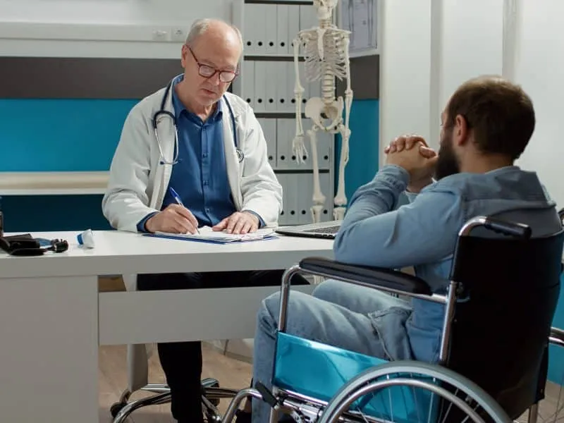 Health specialist doing consultation with wheelchair user in disability friendly cabinet. Medic examining patient with health condition and impairment, using expertise to talk to paralyzed man.