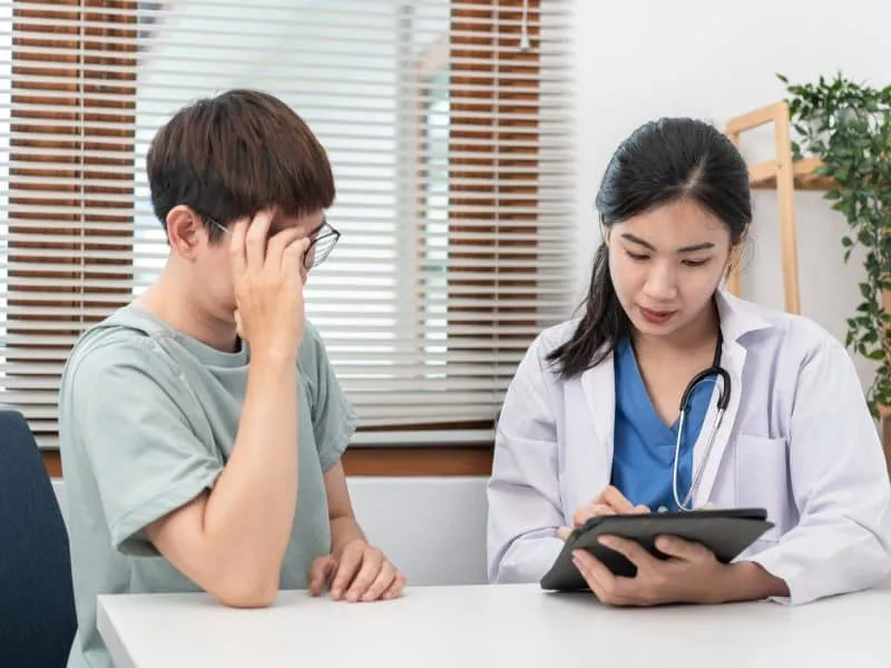 Male patient is feeling headache while female doctor physician is taking notes symptoms on tablet to writing prescription and gives treatment advice in her clinic.