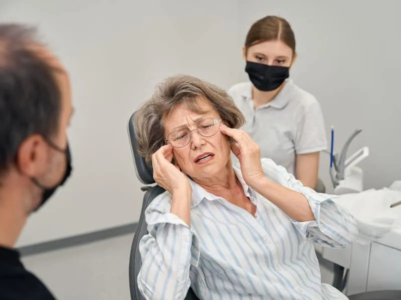 Patient at a dentists appointment complains to a specialist about pain, the doctor works with an assistant