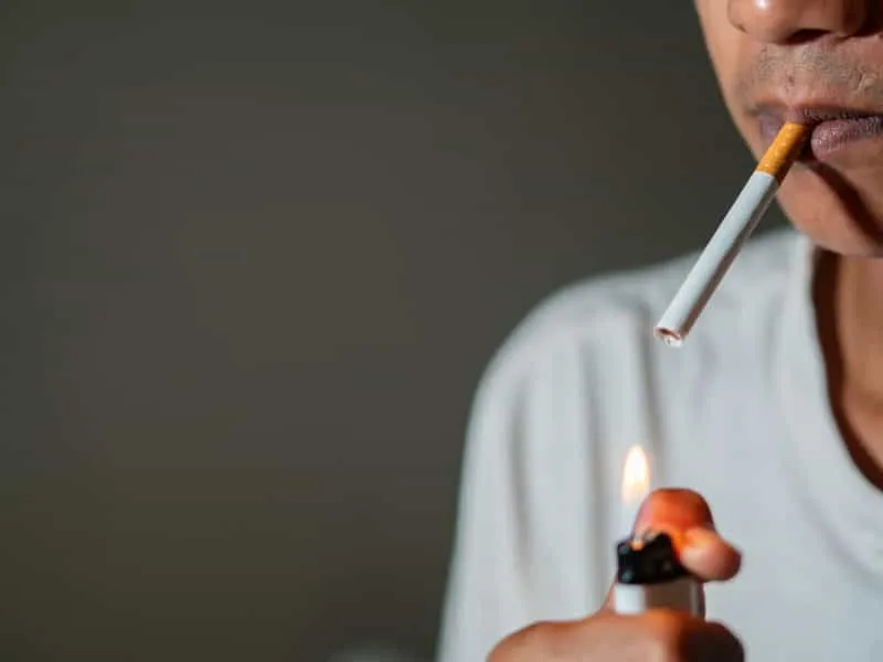 Close-up of a person lighting a cigarette with a lighter.