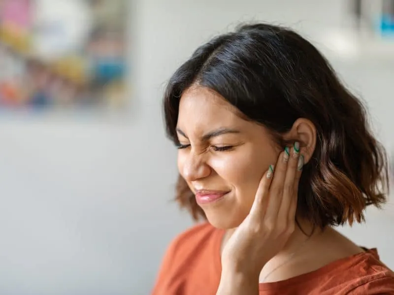 Sick young arab woman having ear pain at home, upset middle eastern female rubbing sore auricle with hand and frowning, suffering from otitis and acute ache, closeup shot with copy space