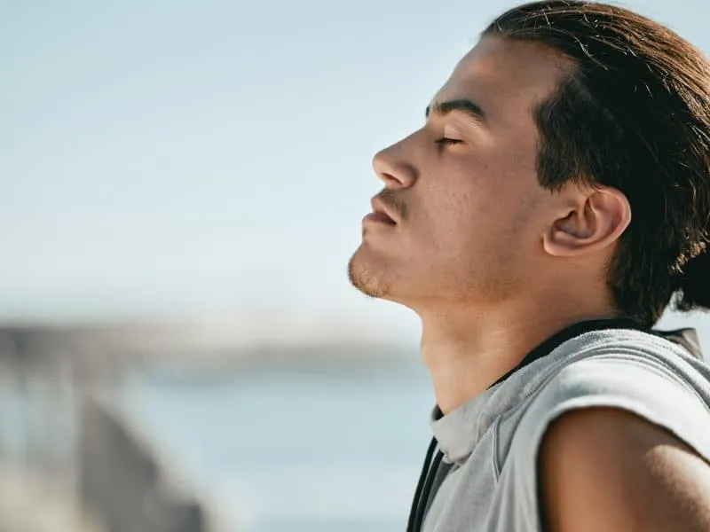 Tired, fitness and breathing man for cardio training, workout or outdoor running break on blue sky .