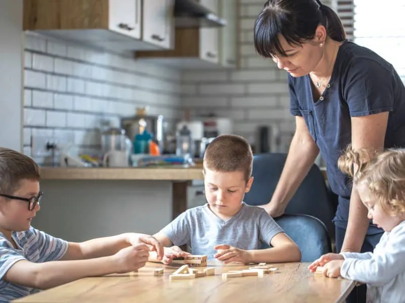 Little children play board game with wooden cubes at home in the kitchen with mom.