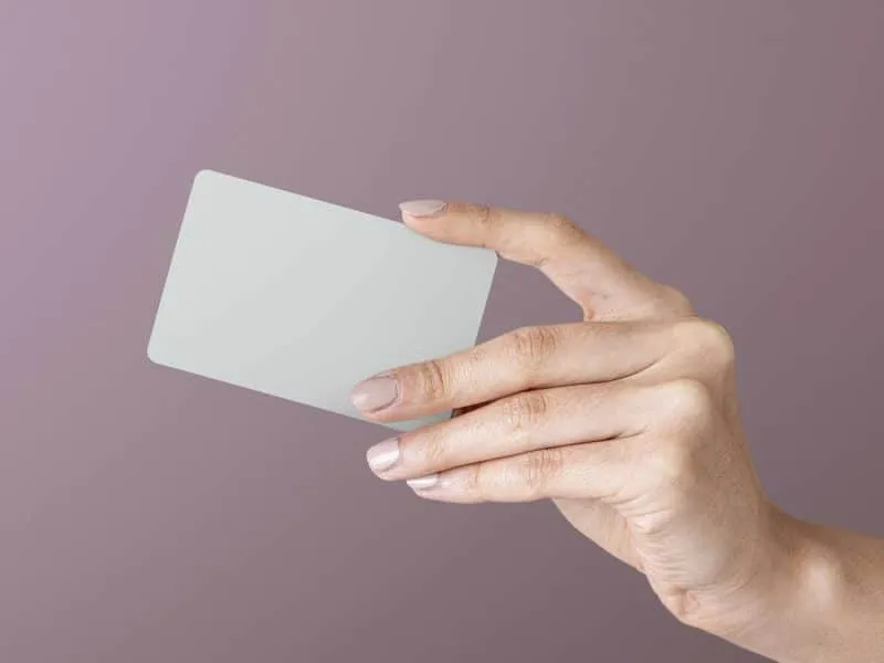 A hand holding a blank, rectangular card against a muted purple background.