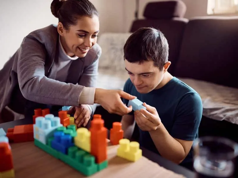 Man with down syndrome enjoying while stacking toy blocks with his psychologist at home.