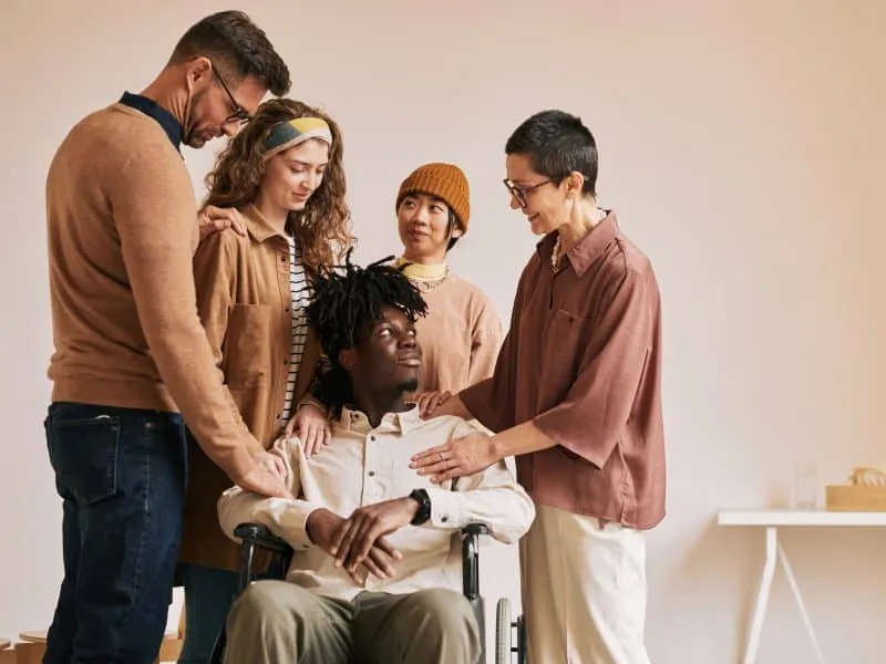 Warm toned portrait of people comforting young man in wheelchair during therapy session in support group, copy space