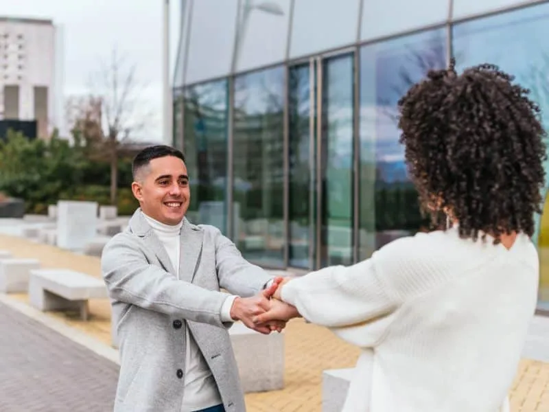 A shallow focus of a young cheerful couple spinning around near a modern building