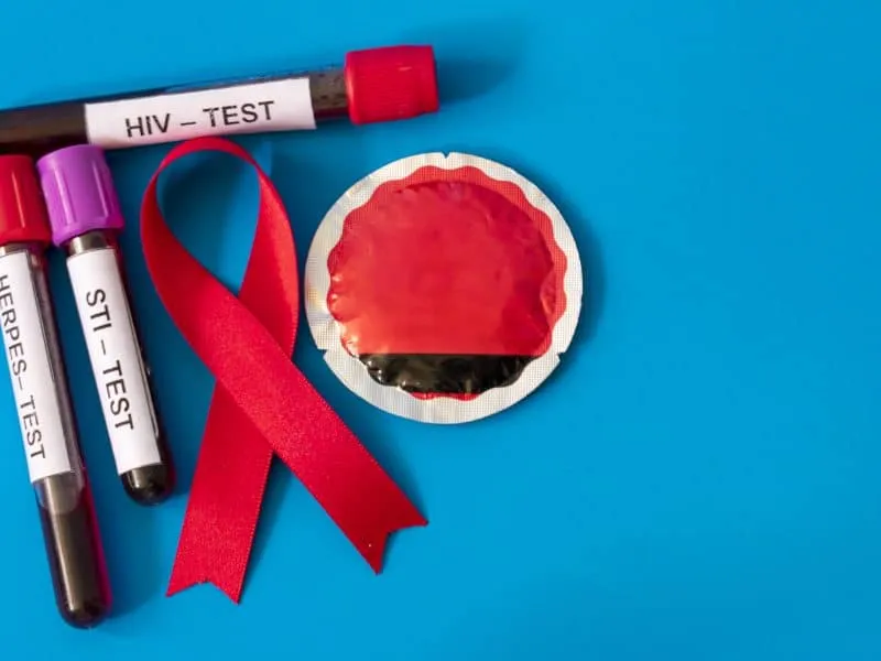 An AIDS ribbon with blood tubes from sexually transmitted disease tests and condom on blue background