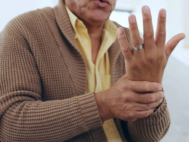 Hand, wrist pain and injury with an elderly person on a sofa in the living room of a home to massag.