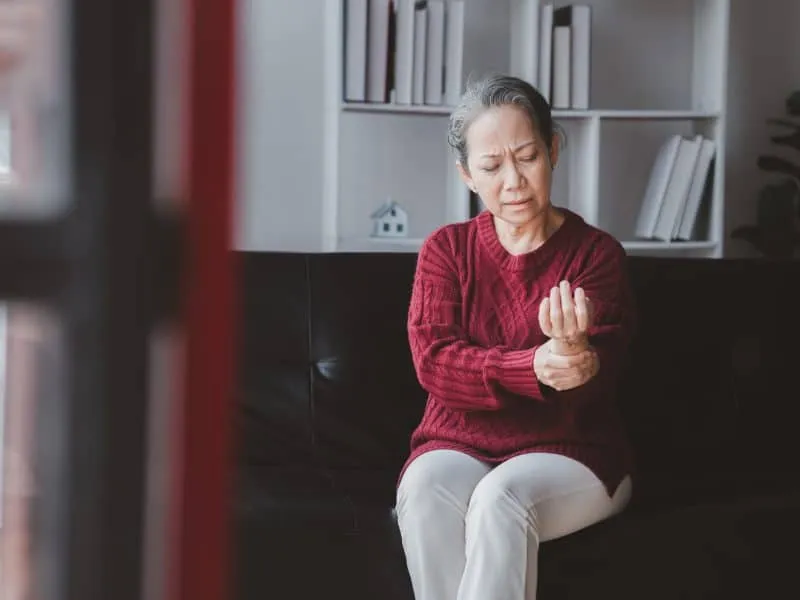 Senior woman sitting in the living room at home and showing body aches, aging sickness, body aches of elderly people, organ degeneration.