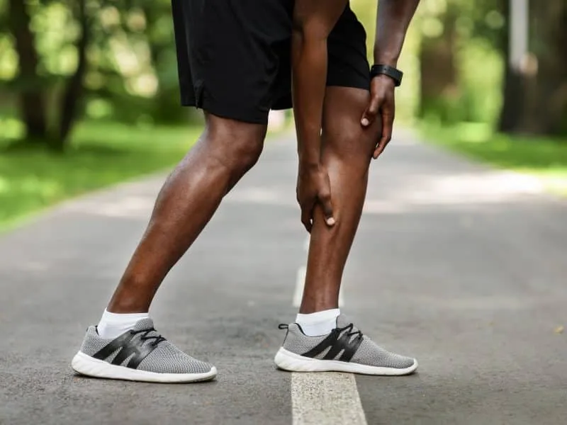 Sport injuries concept. African sportsman massaging leg, feeling pain after running by park, cropped, empty space