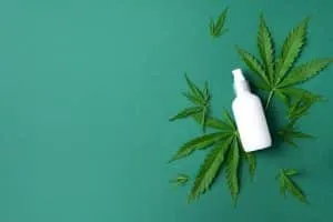Hemp cosmetic products white bottles with oil, hemp seed extract, cream and cannabis leaves on green background. Flat lay. Top view. Copy space. Natural skin care and body treatment.