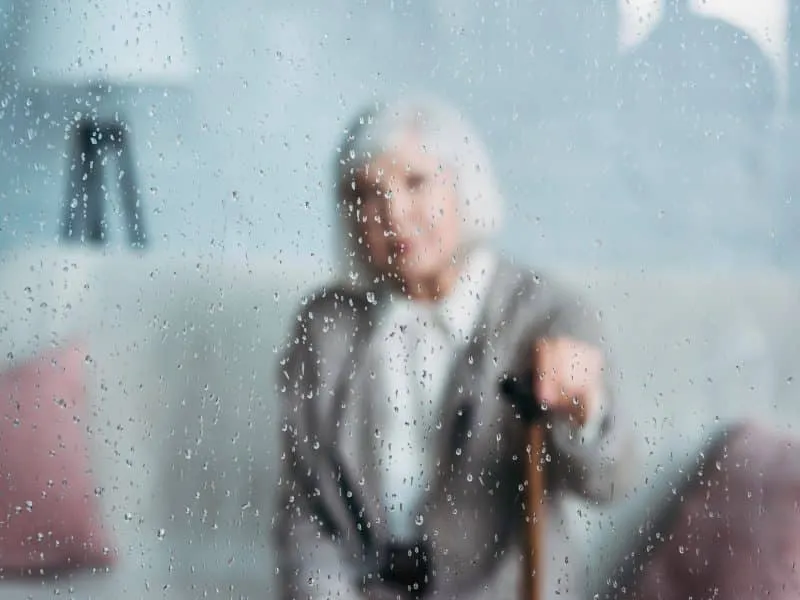 selective focus of grey hair lady with walking stick resting on sofa at home