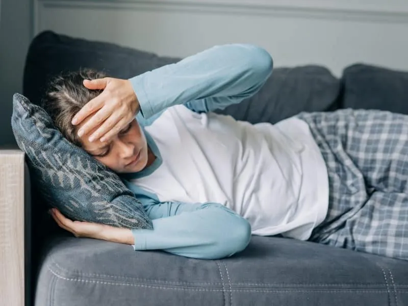 A sick woman with a headache lies on the sofa.