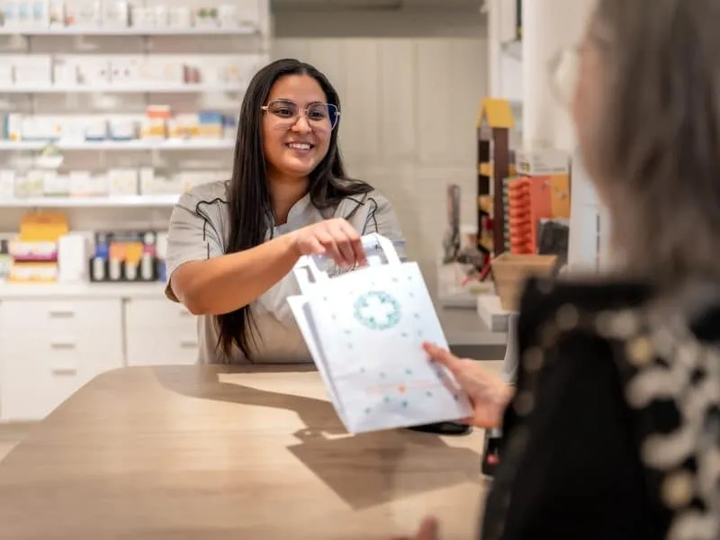 Pharmacist giving medicine into paper bag to a customer at the counter