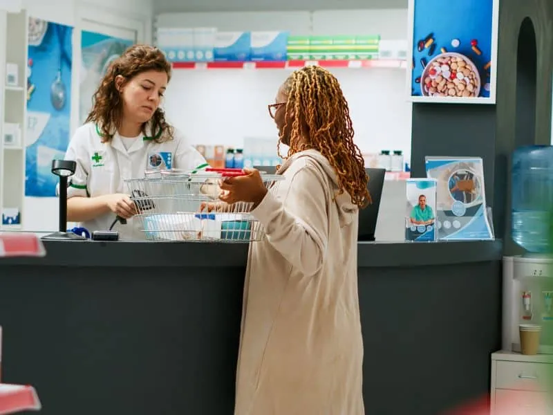 African american client buying pharmaceutical products and medical packages at drugstore counter, pharmacist selling medicine and treatment. Person paying for pills in pharmacy. Handheld shot.