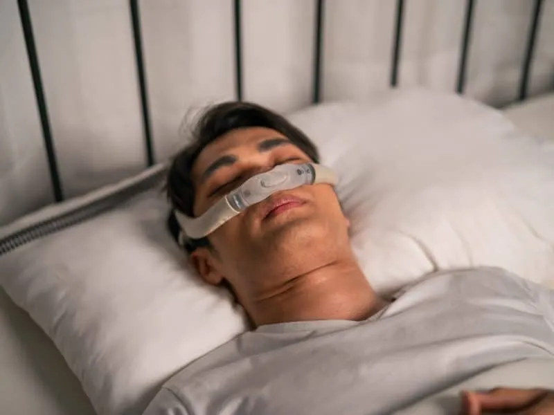 Asian man wearing cpap machine sleeping smoothly all night in bedroom. Attractive handsome healthy male feel happy and relax while lying down on bed, using sleep apnea oxygen mask therapy equipment.
