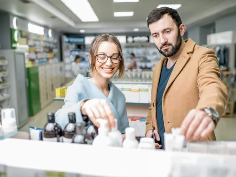 Young couple dressed in coats choosing medicine standing with box in the pharmacy store