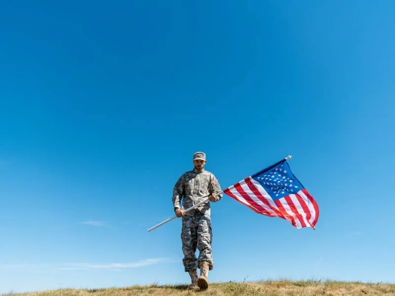 handsome soldier in uniform walking with american flag