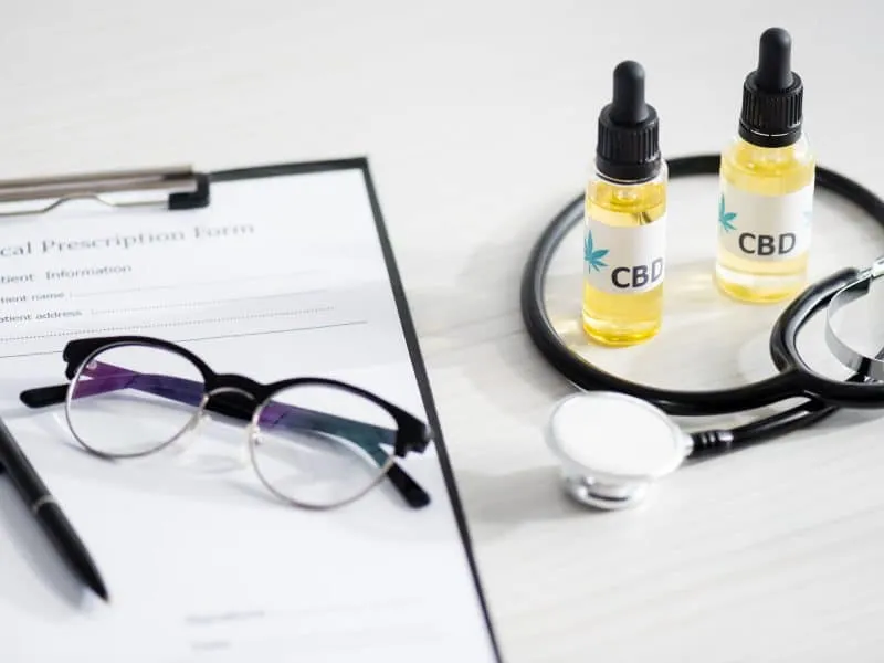 selective focus of bottles with cbd lettering near stethoscope, glasses and clipboard with medical