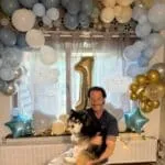 Pomsky - sky 6 Man houdt een kleine husky puppy vast voor een feestdecoratie met ballonnen.
